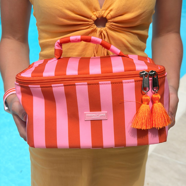 Person holding a orange and pink striped vanity case with tassels against a blue background