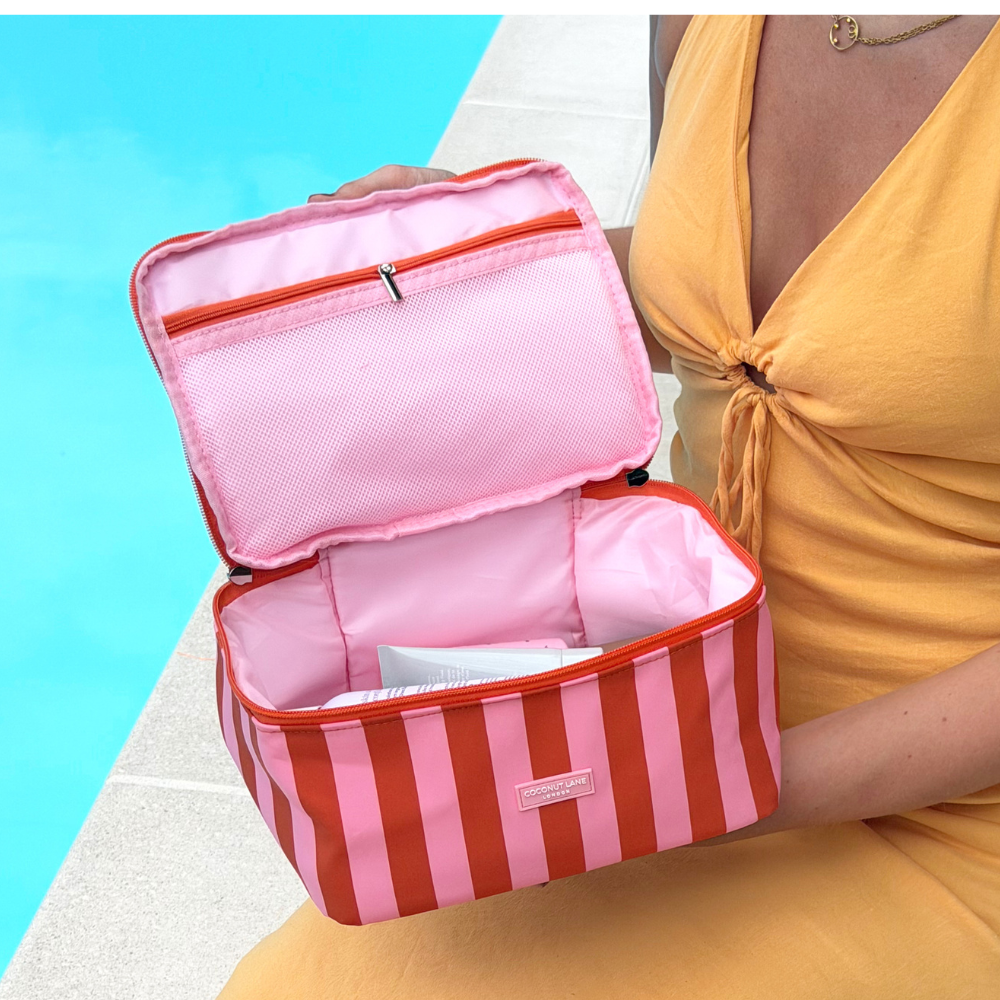 Person holding a pink and orange striped travel vanity case against a blue background