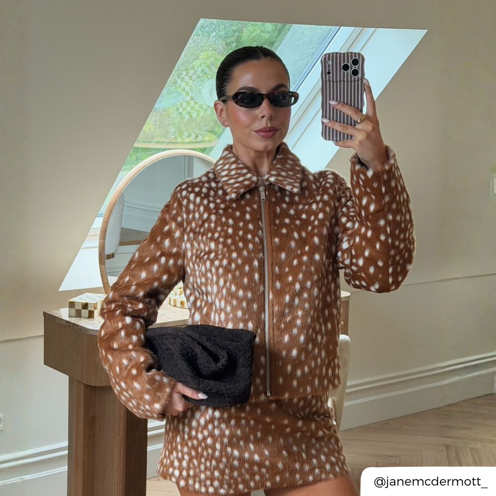 Woman taking a mirror selfie, wearing a faux fawn print co-ord, holding an iphone in a wavy brown and white vertical striped phone case. 