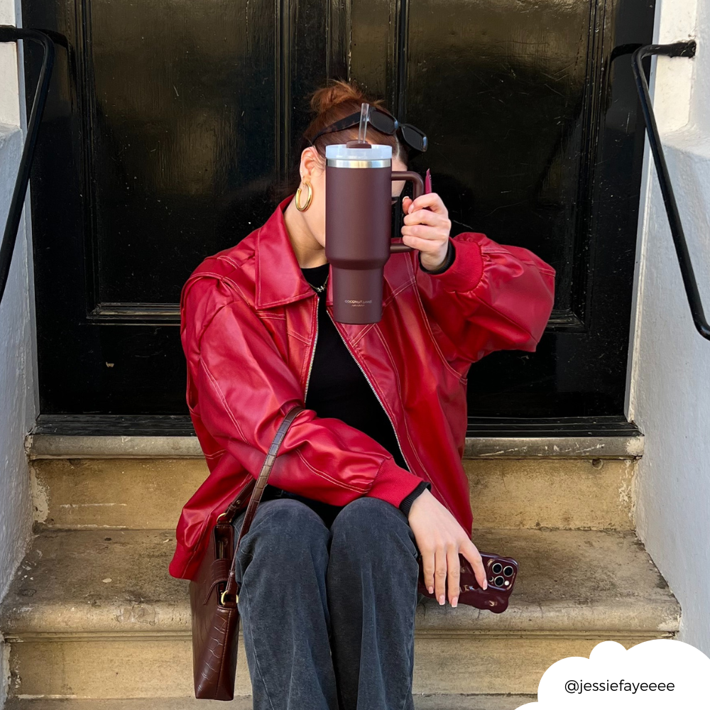 Person in a red jacket on steps holds a burgundy stainless steel tumbler and a phone.