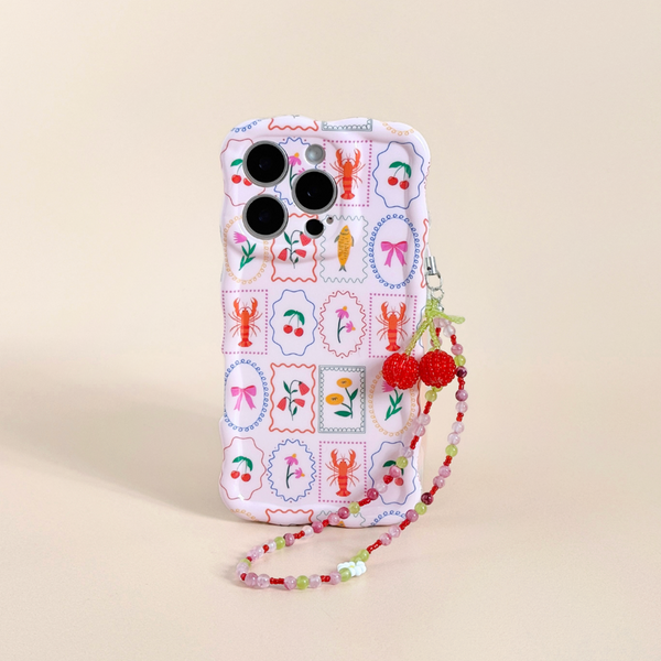 Cherry Bomb Beaded Phone Strap with a cherry charm attached to a pink iPhone case with a stamp pattern.