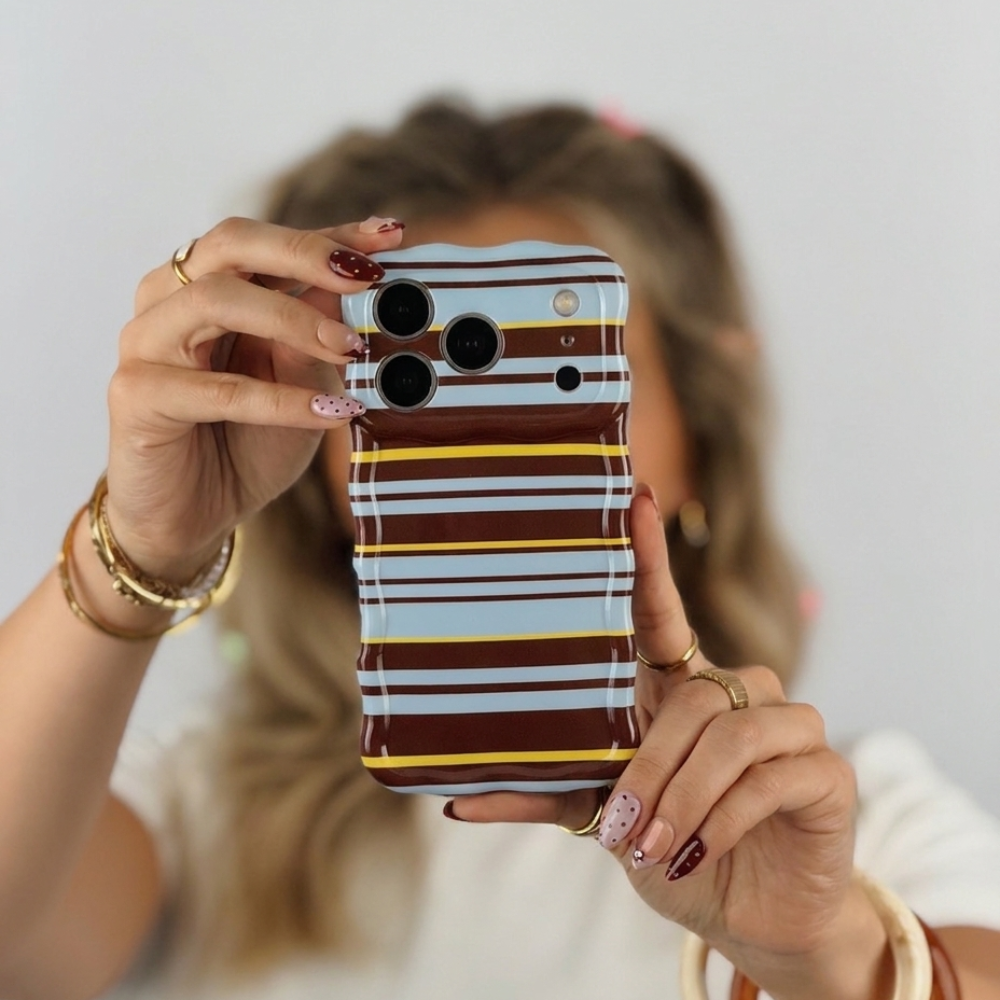 Woman holding a wavy retro mary-kate stripes phone case. The phone case has blue, brown and yellow horizontal lines.