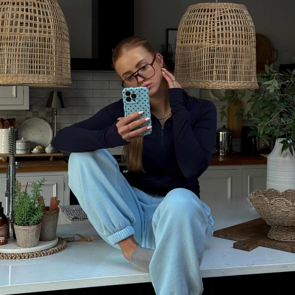 Girl sat on kitchen counter with cool sunglasses holding wavy blue polka phone case.